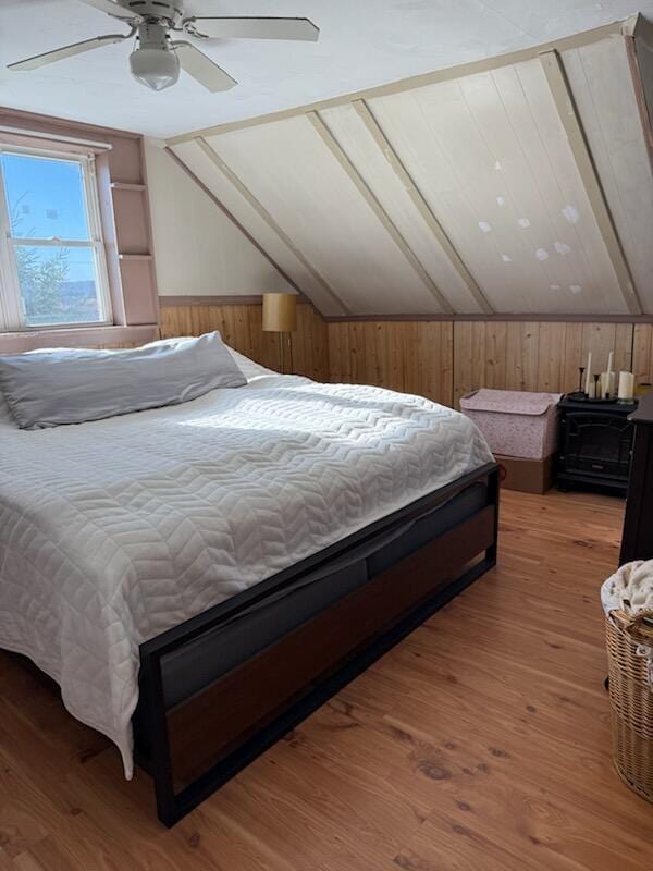 bedroom featuring wood walls, a ceiling fan, vaulted ceiling, and wood finished floors