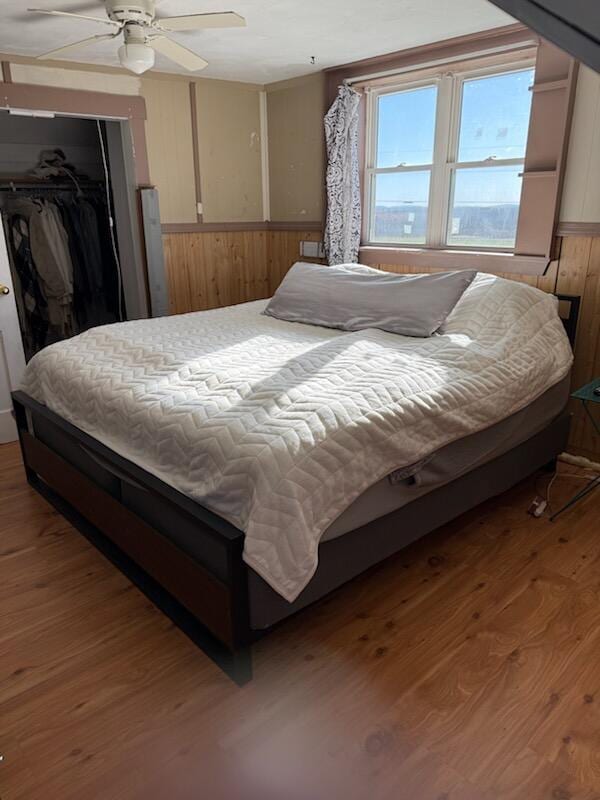 bedroom with ceiling fan, a closet, wood walls, and hardwood / wood-style flooring