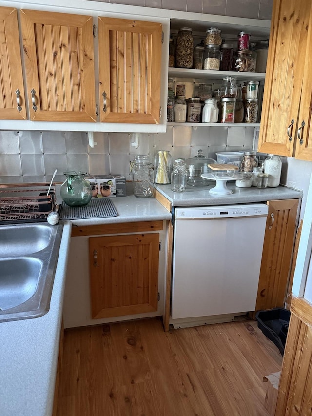 kitchen featuring decorative backsplash, dishwasher, light countertops, light wood-style floors, and a sink