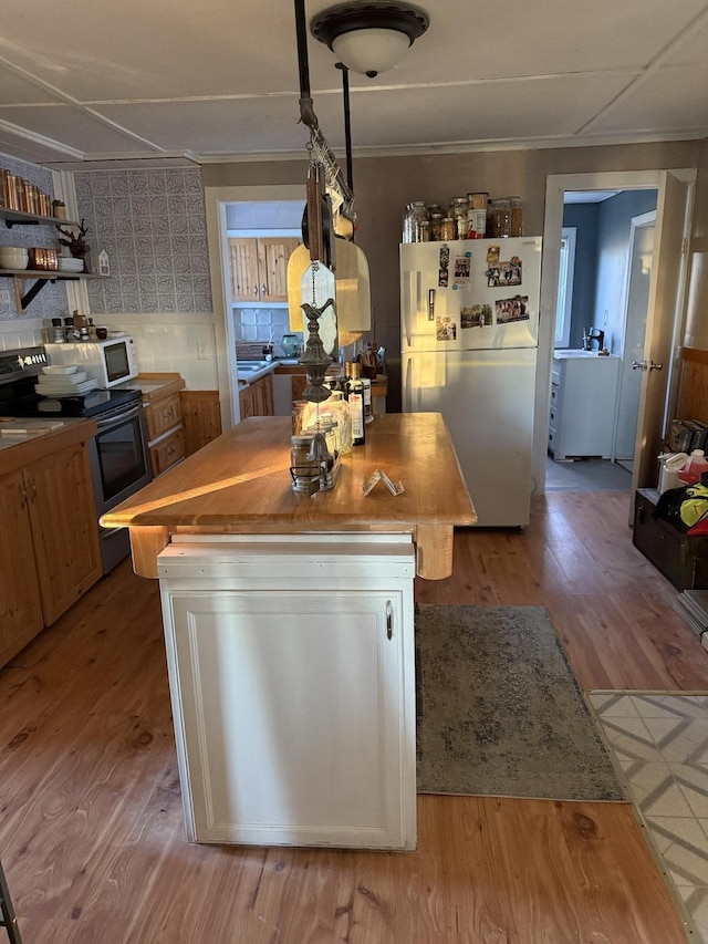 kitchen featuring light wood-type flooring, wood counters, a kitchen island, and white appliances