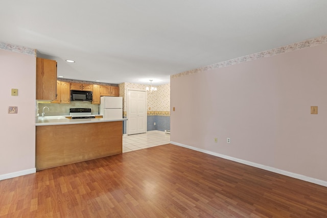 kitchen with white fridge, light hardwood / wood-style flooring, kitchen peninsula, range with electric stovetop, and a notable chandelier