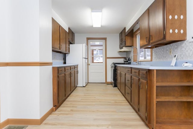 kitchen with light hardwood / wood-style floors, stainless steel range with gas stovetop, backsplash, and white fridge