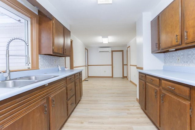 kitchen featuring sink, a wall mounted AC, light hardwood / wood-style flooring, and tasteful backsplash