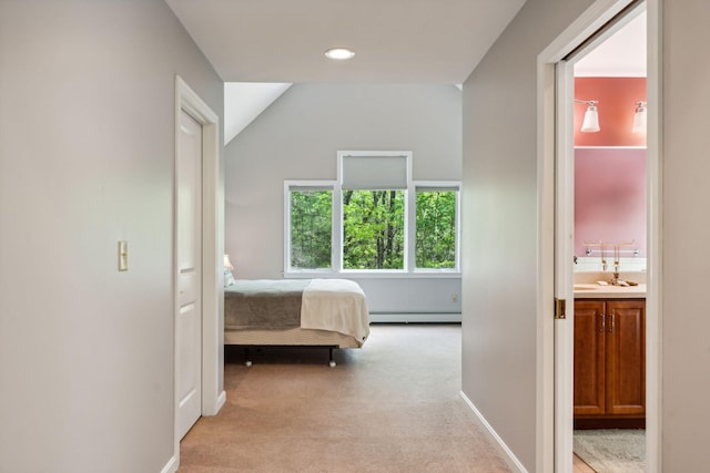 unfurnished bedroom featuring light colored carpet, a baseboard heating unit, sink, ensuite bathroom, and lofted ceiling