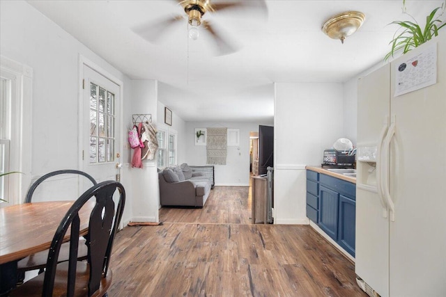 kitchen featuring ceiling fan, dark hardwood / wood-style flooring, blue cabinetry, and white refrigerator with ice dispenser