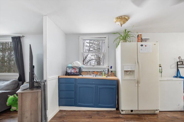 kitchen featuring dark wood-type flooring, white fridge with ice dispenser, blue cabinetry, and sink