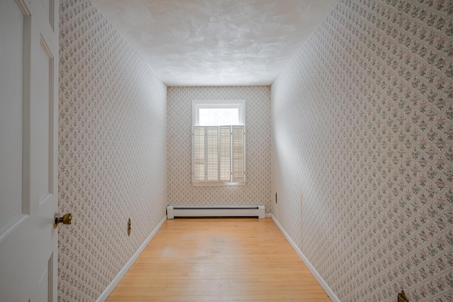 empty room with a baseboard heating unit, light wood-type flooring, and a textured ceiling