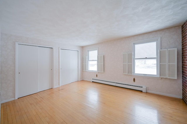 unfurnished bedroom featuring multiple closets, baseboard heating, light hardwood / wood-style flooring, and multiple windows