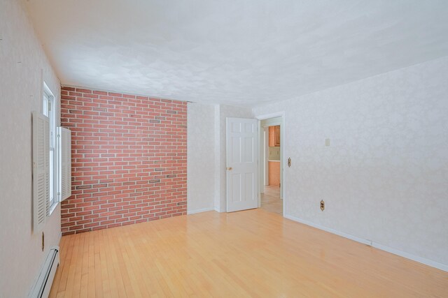 unfurnished room with brick wall, baseboard heating, and light hardwood / wood-style flooring