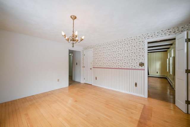 empty room featuring a baseboard heating unit, an inviting chandelier, and hardwood / wood-style flooring