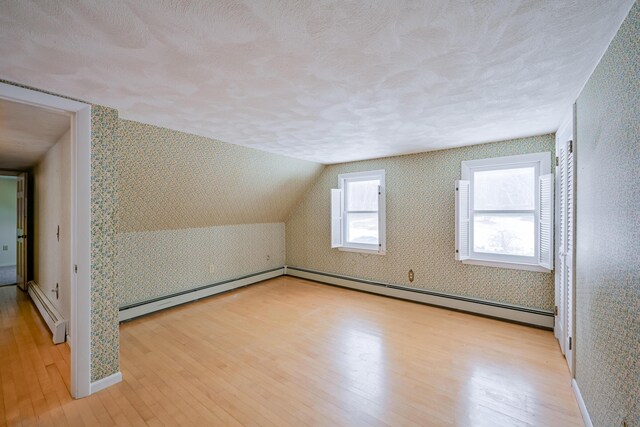 bonus room with a textured ceiling, vaulted ceiling, a baseboard radiator, and light hardwood / wood-style flooring