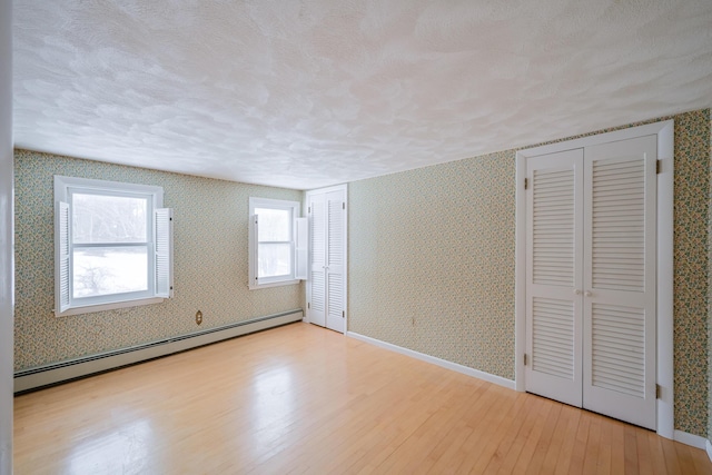 unfurnished bedroom featuring a textured ceiling, a baseboard heating unit, light hardwood / wood-style floors, and multiple closets