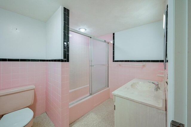 full bathroom with tile walls, shower / bath combination with glass door, vanity, and toilet