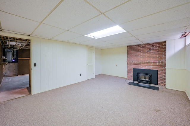 basement featuring carpet floors, a wood stove, and a paneled ceiling