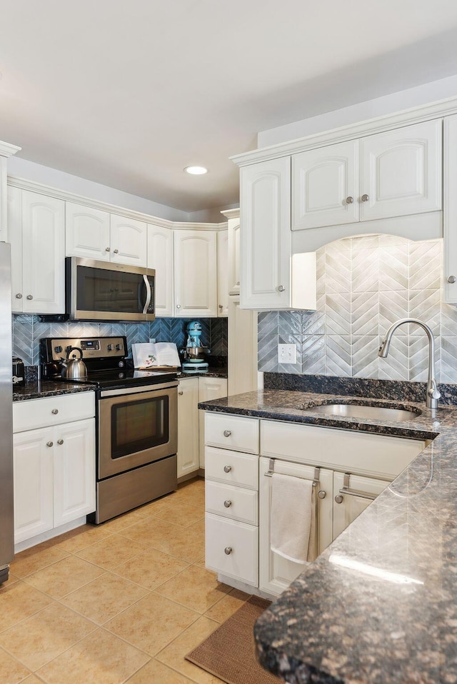 kitchen featuring white cabinets, dark stone countertops, stainless steel appliances, light tile patterned floors, and sink