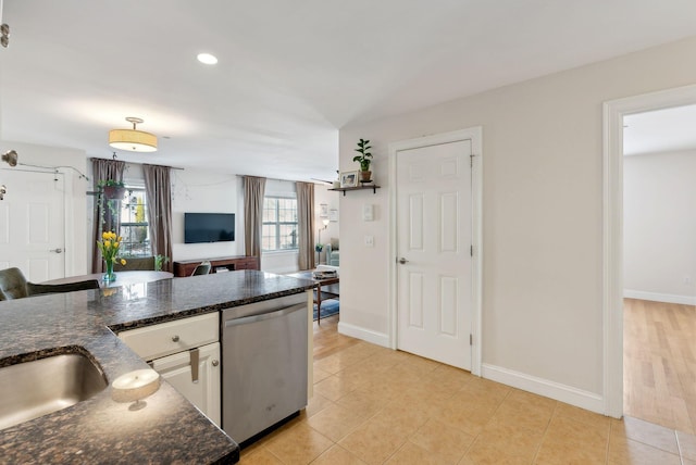 kitchen featuring stainless steel dishwasher, white cabinetry, light tile patterned floors, and dark stone counters