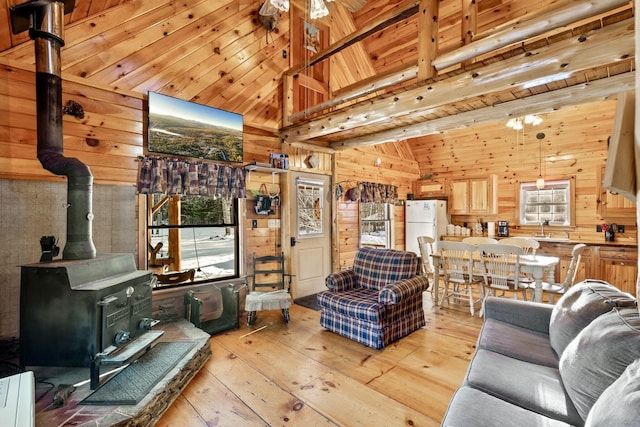 living room with wood walls, light hardwood / wood-style floors, beamed ceiling, a wood stove, and sink