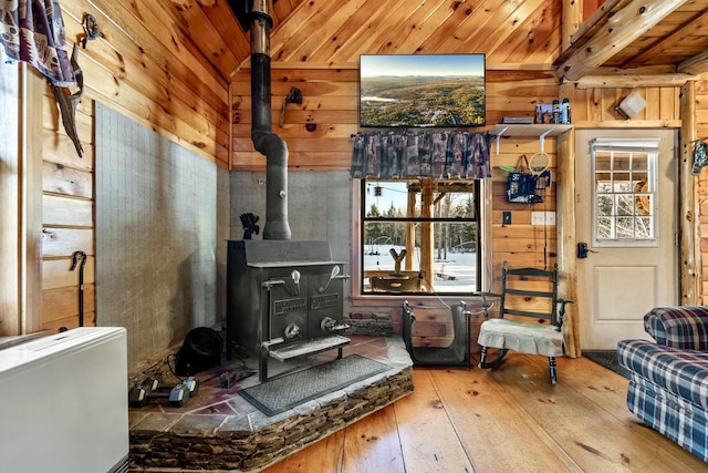 interior space with wooden ceiling, wooden walls, a wood stove, and hardwood / wood-style floors