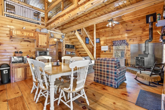 dining space featuring a wood stove, ceiling fan, light hardwood / wood-style flooring, wood ceiling, and beam ceiling