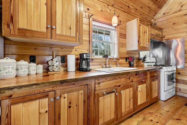 kitchen with wooden walls, gas range gas stove, hanging light fixtures, and sink