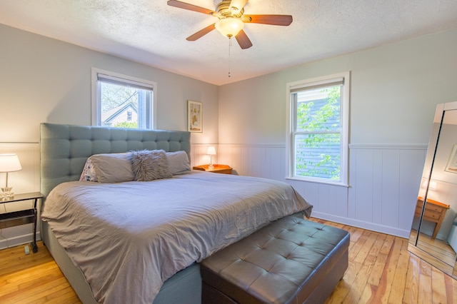 bedroom featuring multiple windows, light wood-style floors, a wainscoted wall, and a textured ceiling