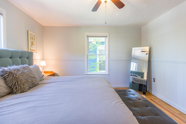 bedroom with ceiling fan, a wainscoted wall, and wood finished floors