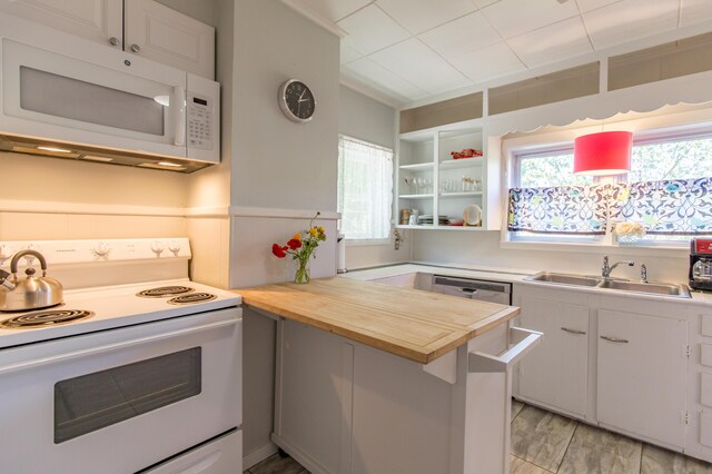 kitchen with a sink, white appliances, white cabinets, light wood finished floors, and wooden counters