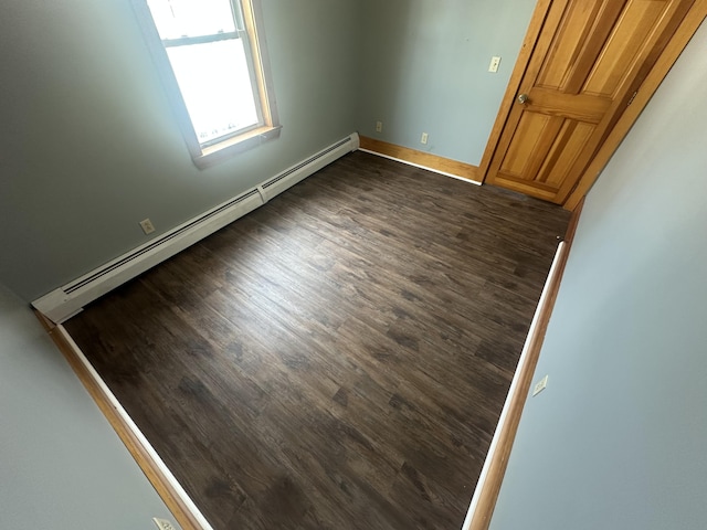 unfurnished room featuring dark wood-type flooring and a baseboard heating unit