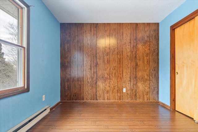 empty room featuring a baseboard radiator, wood walls, and wood-type flooring