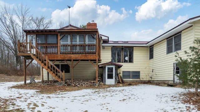 snow covered rear of property featuring a sunroom