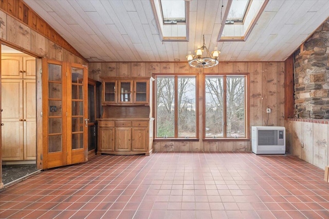 interior space featuring an inviting chandelier, wood walls, vaulted ceiling with skylight, and heating unit