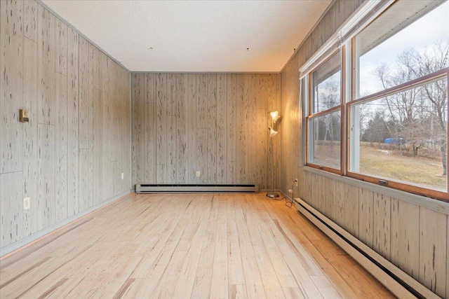 unfurnished room with light hardwood / wood-style flooring, wooden walls, and a baseboard heating unit