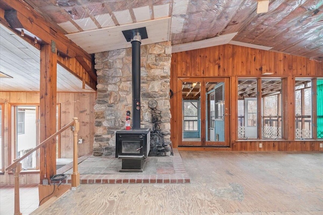 unfurnished living room with wood walls, lofted ceiling, and a wood stove