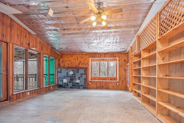 unfurnished living room featuring wooden walls, ceiling fan, and a wood stove