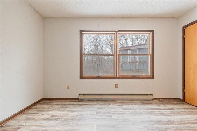 spare room featuring baseboard heating and light hardwood / wood-style flooring