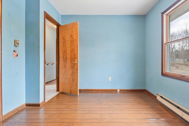 unfurnished bedroom with baseboard heating, light wood-type flooring, and multiple windows