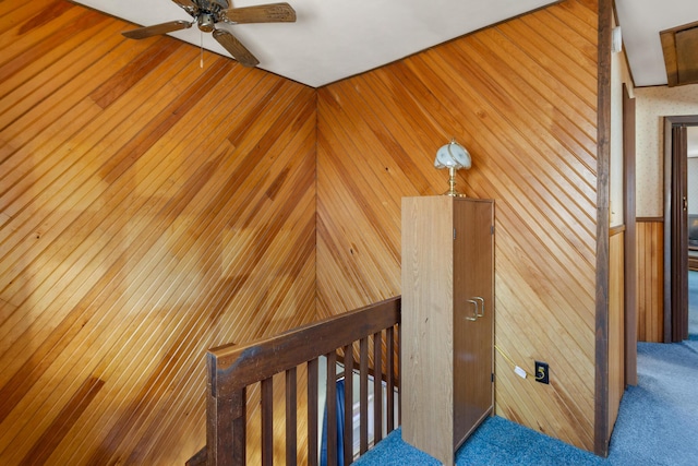 stairs featuring wood walls, ceiling fan, and carpet