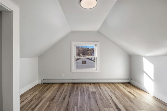 additional living space with lofted ceiling, a baseboard heating unit, and light hardwood / wood-style flooring