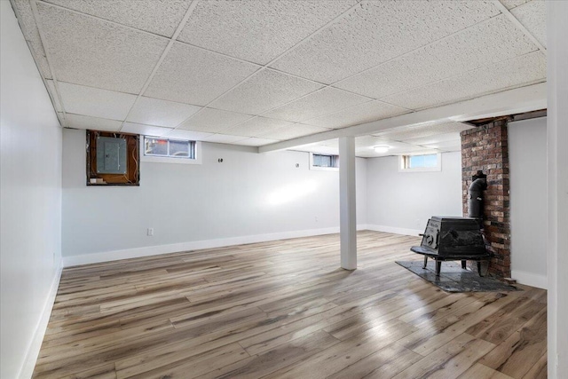 basement with electric panel, a paneled ceiling, a wood stove, and hardwood / wood-style floors