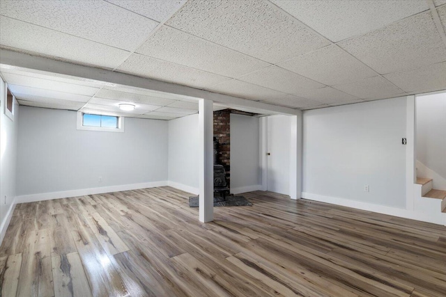 basement featuring a paneled ceiling, a wood stove, and hardwood / wood-style flooring