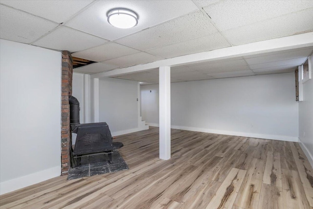 basement with hardwood / wood-style flooring, a drop ceiling, and a wood stove