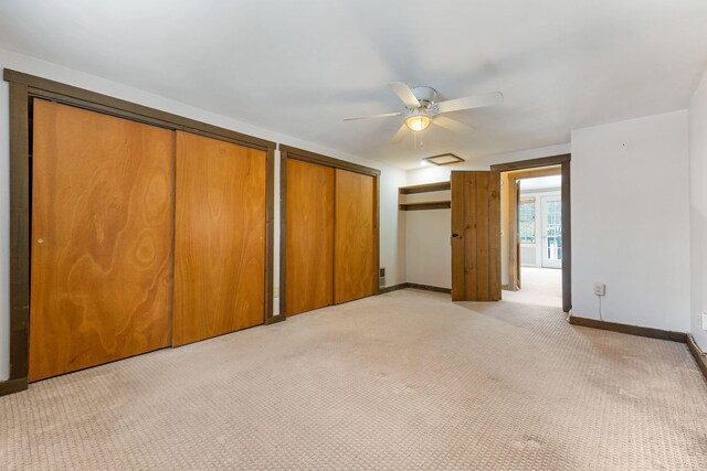 unfurnished bedroom featuring light colored carpet, ceiling fan, and multiple closets