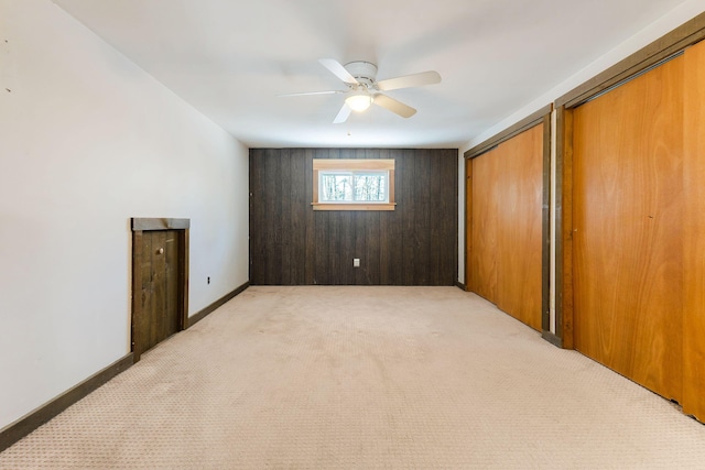 interior space with light carpet, wood walls, ceiling fan, and two closets