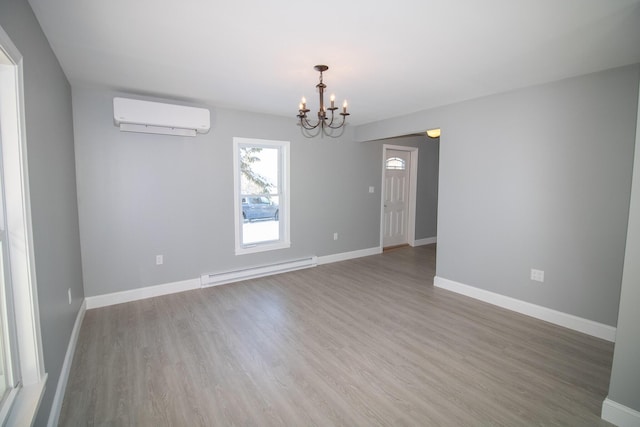 unfurnished room with hardwood / wood-style flooring, baseboard heating, a wall unit AC, and a notable chandelier