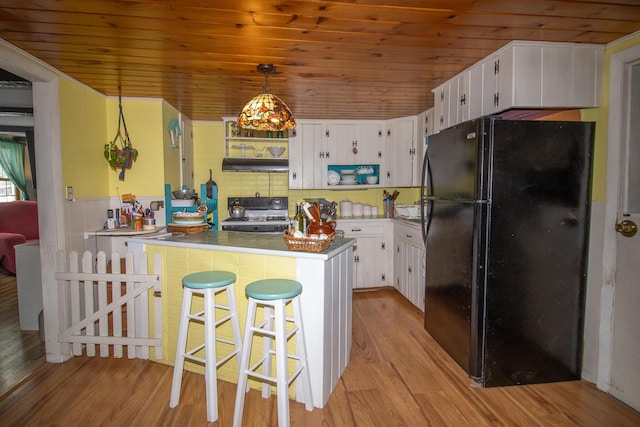 kitchen with decorative light fixtures, white cabinetry, black refrigerator, a kitchen breakfast bar, and range