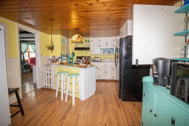 kitchen featuring pendant lighting, black refrigerator, light wood-type flooring, white cabinetry, and a kitchen breakfast bar