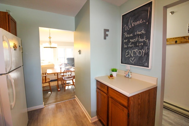 kitchen with a baseboard heating unit, wood finished floors, light countertops, freestanding refrigerator, and brown cabinetry