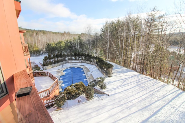 snow covered pool with a fenced in pool, a deck, and a forest view