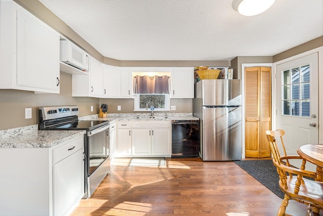 kitchen with sink, a textured ceiling, appliances with stainless steel finishes, hardwood / wood-style floors, and white cabinets