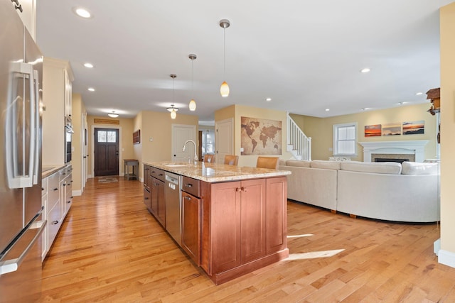 kitchen with pendant lighting, a center island with sink, sink, light stone countertops, and appliances with stainless steel finishes